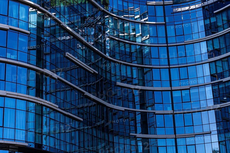 A close-up view of a modern building showcasing a curved glass facade with visible reflections and metal frames, illustrating the use of concrete, glass, and metal in contemporary architecture