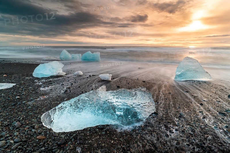 Captivating view of Diamond Beach in Iceland, showcasing stunning ice chunks scattered on the black sand with a breathtaking sunrise illuminating the scene