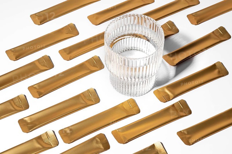 From above a golden jelly collagen sachets arranged on a white background alongside a transparent glass. The sachets are designed for convenient, on-the-go health supplements
