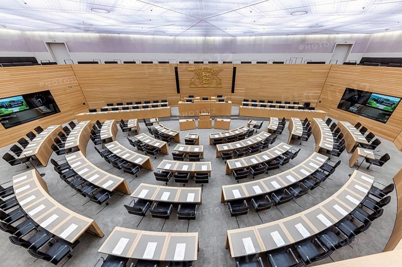Plenary hall deserted with the seats of deputies and the government bank. Behind it is the coat of arms of the federal state. The state parliament of Baden-Württemberg is the state parliament based in Stuttgart, Baden-Württemberg, Germany