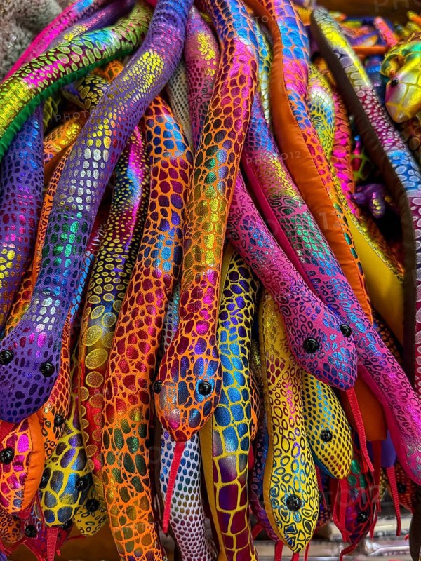 A vibrant collection of colorful plush snakes displayed in a Thai souvenir market. Each snake features unique, bright patterns, reflecting the lively culture of Thailand. Perfect for travelers