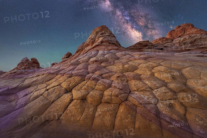 A breathtaking view of the Milky Way illuminating a unique, textured rock formation in Coyote Buttes, Arizona. The night sky is filled with stars, showcasing nature wonder