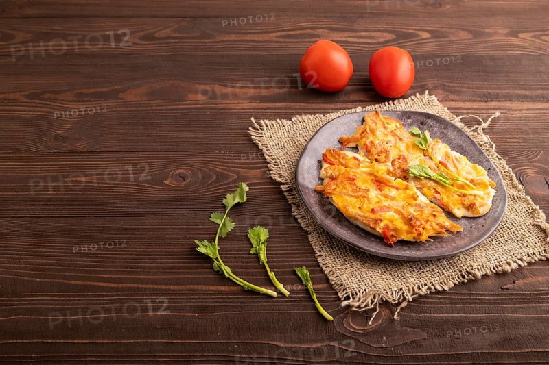 Baked chicken meat with cheese and tomatoes on brown wooden background and linen textile. side view, copy space
