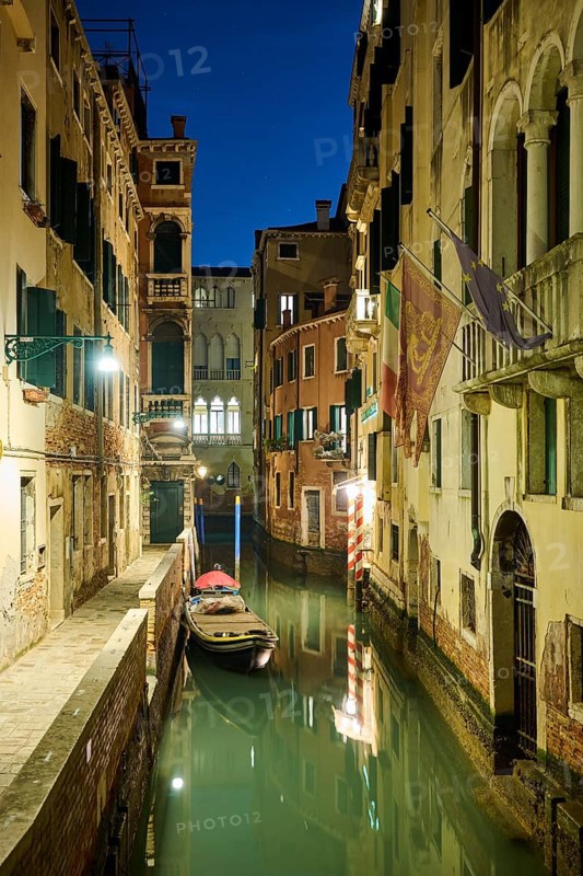 View on a waterway with a boat lying in the water in Venice by night in winter, Italy