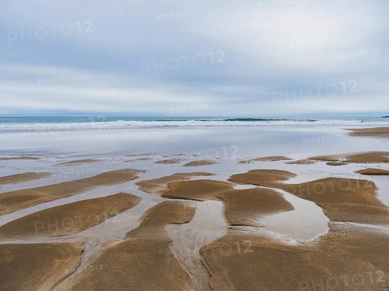 Serene coastal landscape featuring expansive sandy shores and reflective tidal pools under a cloudy sky, conveying the beauty and calm of nature