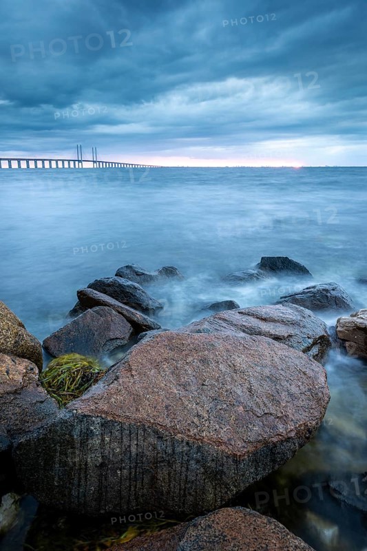 Rocks in the foreground lead to a bridge running across the sea in the distance, Öresund Bridge, Øresundsbroen, the world's longest cable-stayed bridge, connecting Copenhagen with Malmö