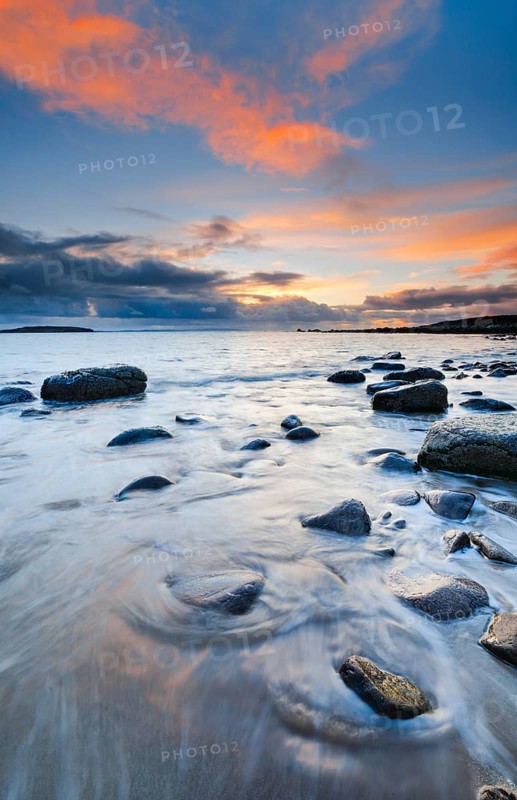 Orange coloured cloudy sky at sunset on a sandy beach strewn with round stones near Achiltibuie on the west coast of Scotland