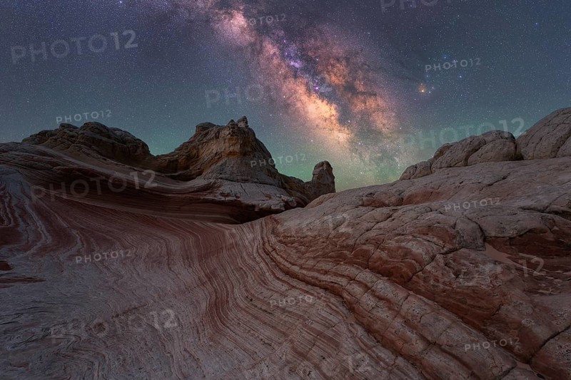 Experience the breathtaking Milky Way shining over the unique rock formations of White Pocket in Arizona's desert. This stunning nightscape captures the serene beauty of the cosmos