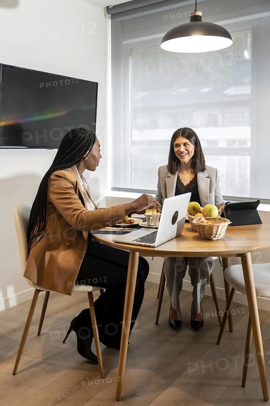 Two businesswomen are enjoying breakfast and working together in a hotel room during a business trip