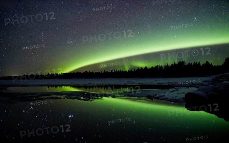 Aurora borealis in green colors over lake in snow covered landscape at night, Lapland, Finland