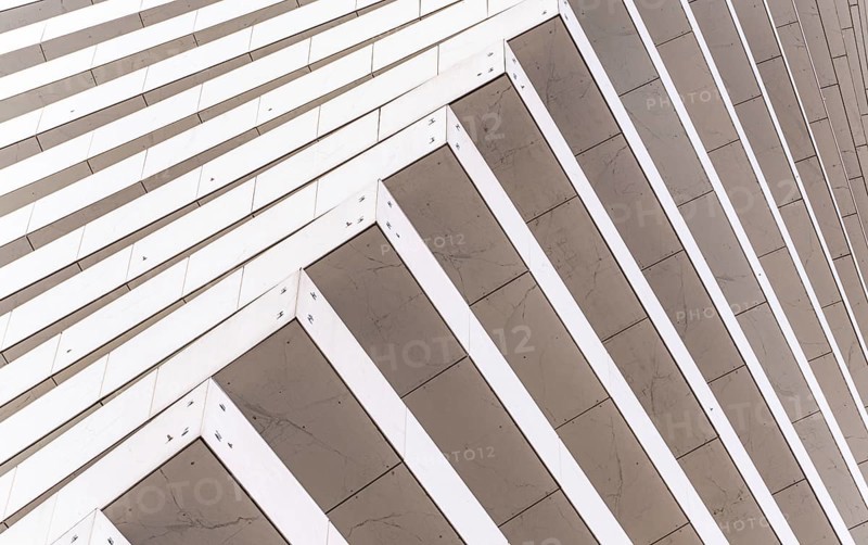 Close-up of a modern architectural facade featuring diagonal lines creating a dynamic pattern. The light and shadow interplay highlights the building's contemporary design