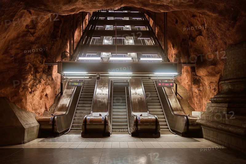 View of escalators at a Stockholm subway station, surrounded by cave-like rock formations. The station design blends urban architecture with natural elements for a unique visual effect