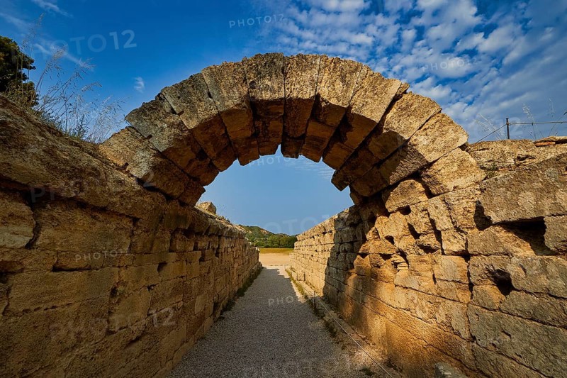 Crypt, vaulted walkway to the stadium, old stone arch leading through massive walls under a blue cloudy sky, Archaeological Site, Ancient Olympia, Peloponnese, Greece