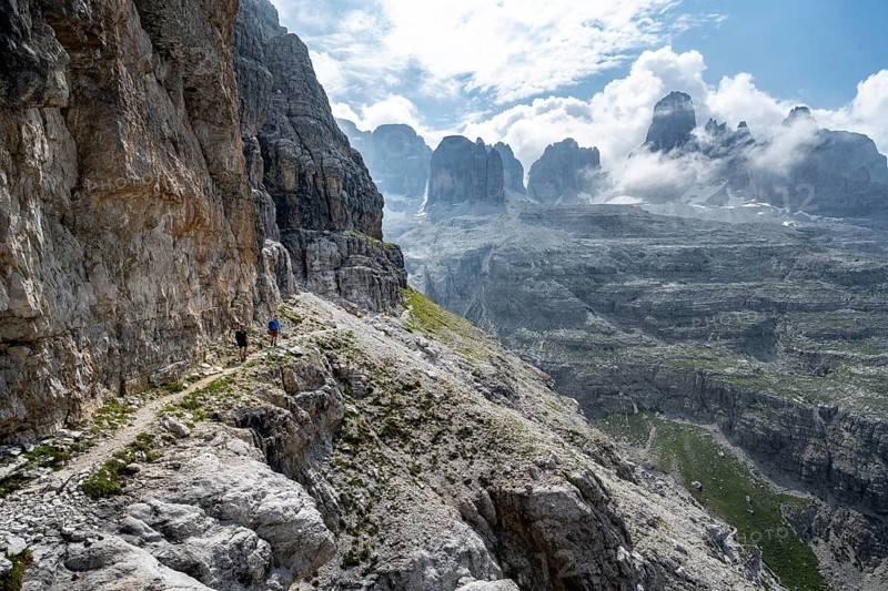 Two mountaineers on a hiking trail in front of a picturesque mountain landscape with rocky peaks, Via Ferrata SOSAT via ferrata, summit of Cima Tosa in the back, Brenta Mountains, Trentino, Italy