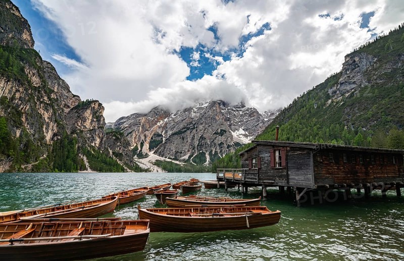 Traditional wooden rowboats rest near a rustic wooden boathouse on Lago di Braies, surrounded by dramatic cliffs and snow-capped peaks in the Dolomites, Italy