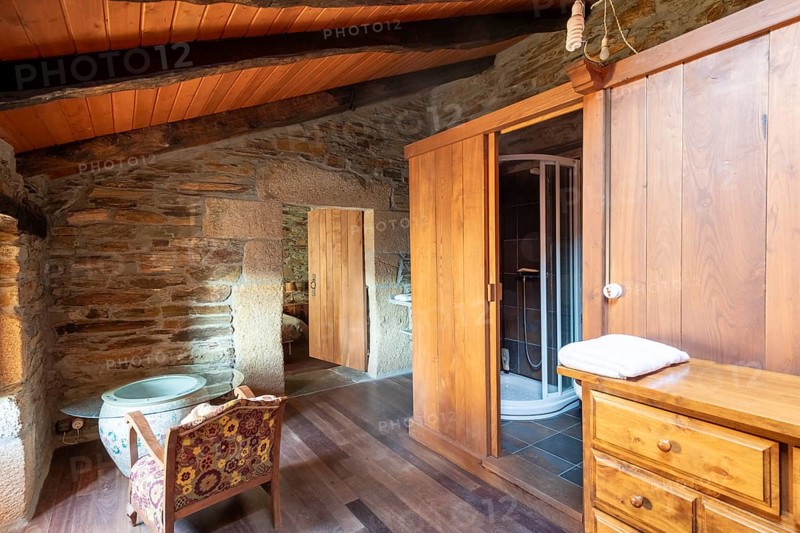 Picture of a charming rustic room inside a country house located in Lugo, Spain, featuring a stone wall, wooden furniture, and a traditional wooden beam ceiling