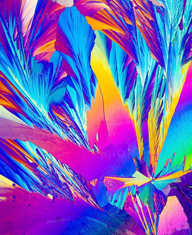 This image captures the stunning microscopic view of Adipic acid crystals, showcasing a vivid array of colors including electric blue, magenta, yellow, and purple. The angular formations highlight the unique crystal structure