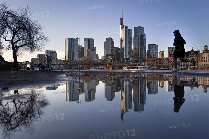 Frankfurt's banking skyline and a jogger running by are reflected in a puddle on the banks of the Main, Frankfurt am Main, Hesse, Germany
