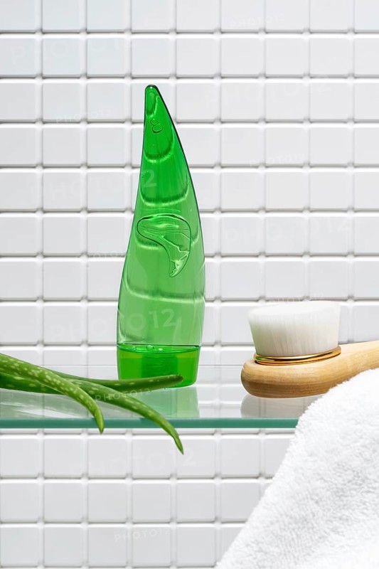 Bathroom essentials for skin care featuring a bottle of aloe vera gel and body cream beside a fresh aloe plant, against a white tile background