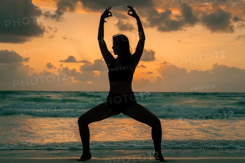 Silhouette of a woman practicing yoga on a beach during sunrise in Tulum, Mexico. The serene atmosphere, coupled with the ocean waves, creates a sense of peace and tranquility
