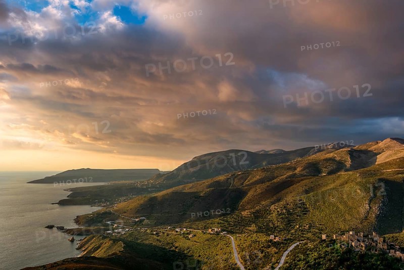 Golden hour view of the rugged hills and coastal villages of the Mani Peninsula, with winding roads and the sea under a spectacular sunset sky, creating a serene Mediterranean landscape
