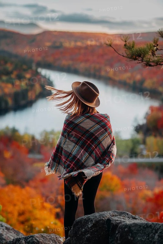 A woman in a hat and plaid shawl stands overlooking a picturesque Quebec landscape in autumn. The vibrant red, orange, and yellow foliage create a stunning view