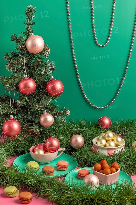 Small Christmas tree with baubles and macaroons in pink and green, surrounded by decorations