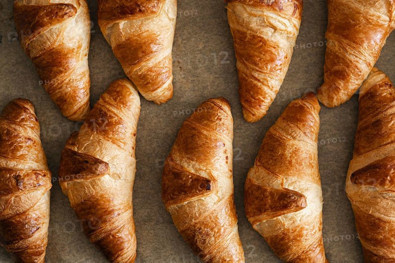 A high angle view of freshly baked homemade croissants placed on a baking sheet. Their golden brown crusts glisten, showcasing the perfect flaky texture and buttery aroma