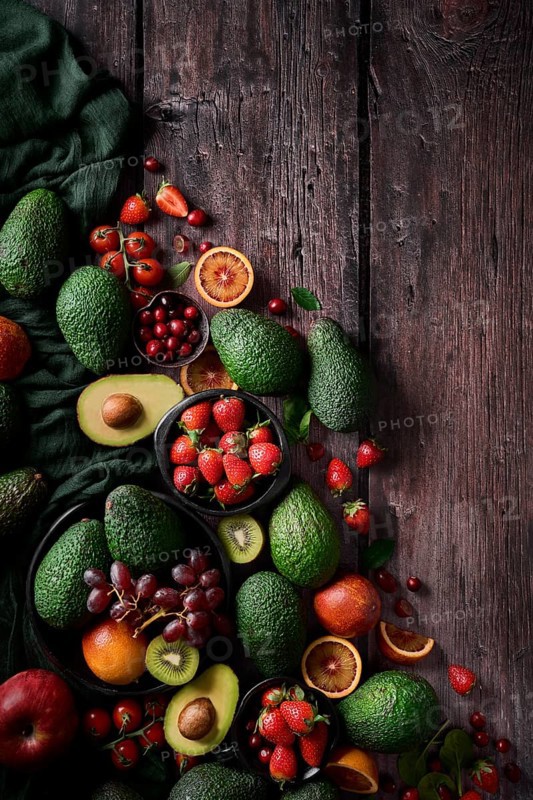 A vibrant assortment of fresh fruits and vegetables, including avocados, strawberries, grapes, and citrus, artfully arranged on a rustic dark wooden table. Perfect for a healthy lifestyle