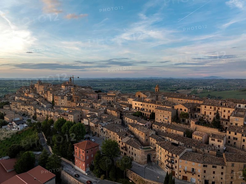 Aerial view of the historic town of Treia in Italy at sunset. The ancient architecture and warm hues create a picturesque scene against the vast countryside backdrop