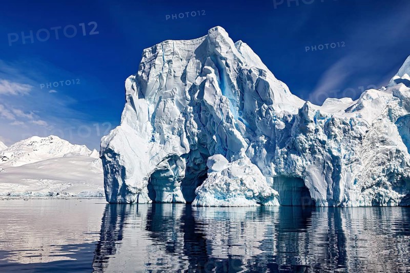Imposing icebergs are reflected in the calm water under a clear blue sky, icebergs in the Southern Ocean in Antarctica