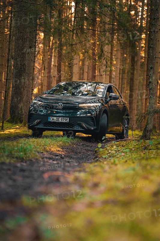 Car on a forest path with grass and light, flanked by tall trees, car sharing vehicle Deer Mobility, electric car VW ID5, Black Forest, Germany