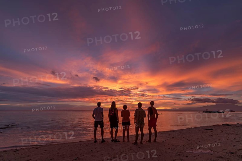 Back view silhouette of unrecognizable friends standing on a beach in the Philippines, watching a stunning sunset with vibrant colors in the sky. Ideal for depicting vacation or holiday scenes