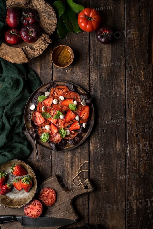Anonymous people preparing a healthy tomato and strawberry salad on a wooden rustic table