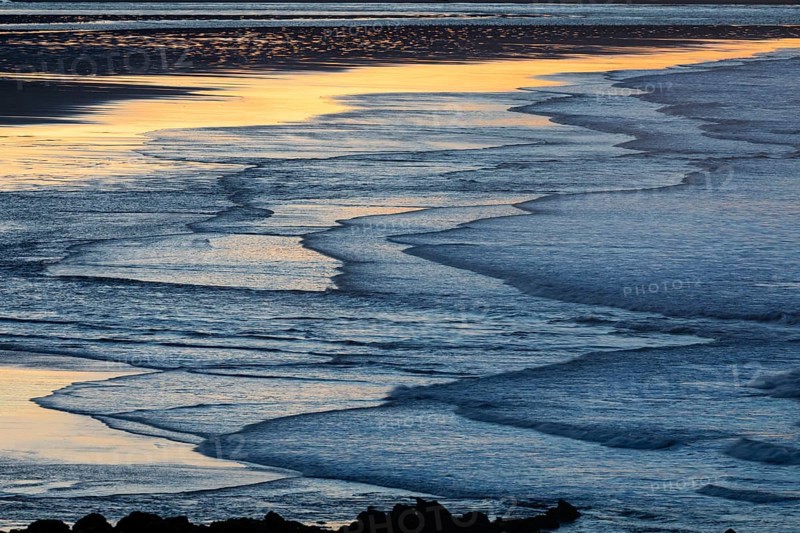Low tide and gentle waves, at dusk on the North Sea, on the North-east coast of Northumberland, England, UK