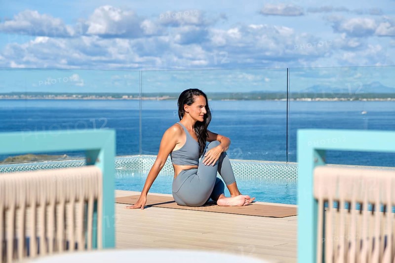 A woman practices yoga on a deck overlooking a vast ocean, enjoying a peaceful environment. The clear sky and tranquil waters create a serene atmosphere