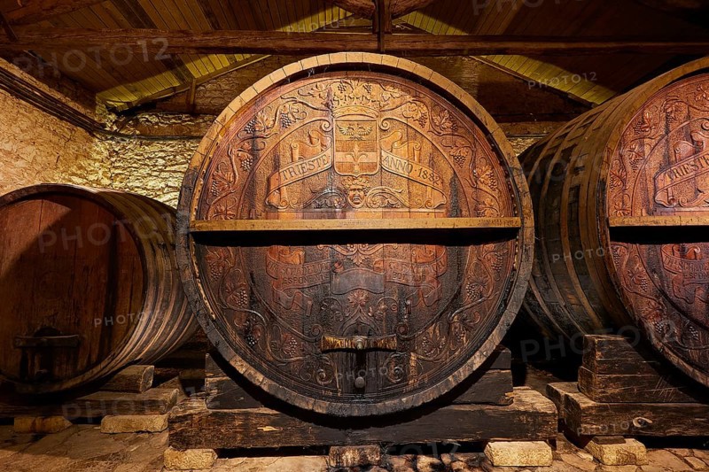 Large wooden barrel with engravings surrounded by stone walls in a wine cellar, Achaia Clauss winery, Patras, Peloponnese, Greece