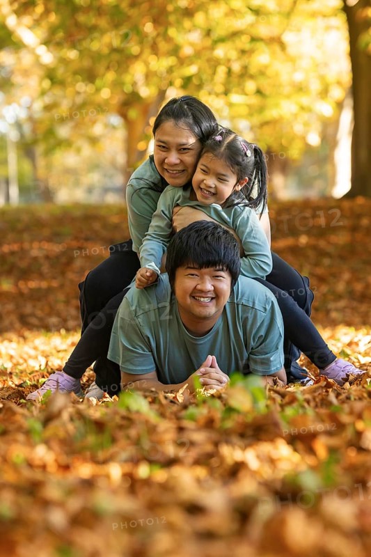 Joyful Asian family laughing and playing together among fallen autumn leaves in a serene park setting, embodying warmth, unity, and the joy of spending time outdoors
