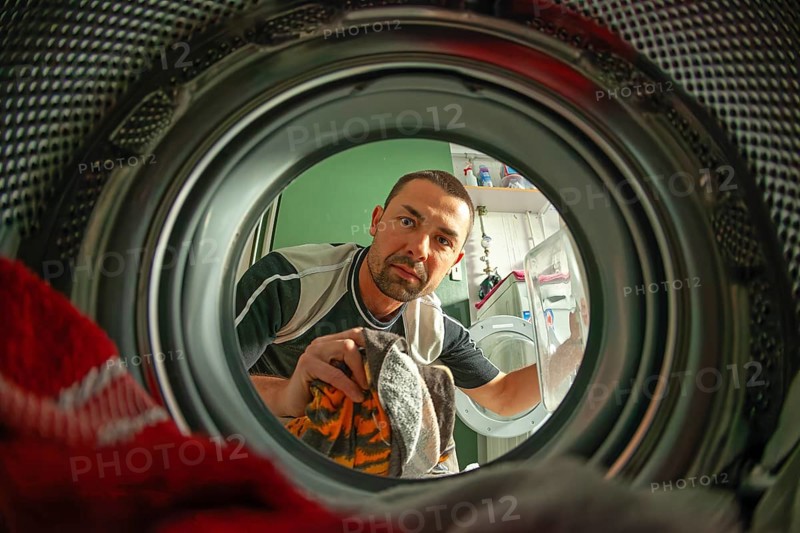 Man loads laundry, looking into washer from inside drum, home chore scene