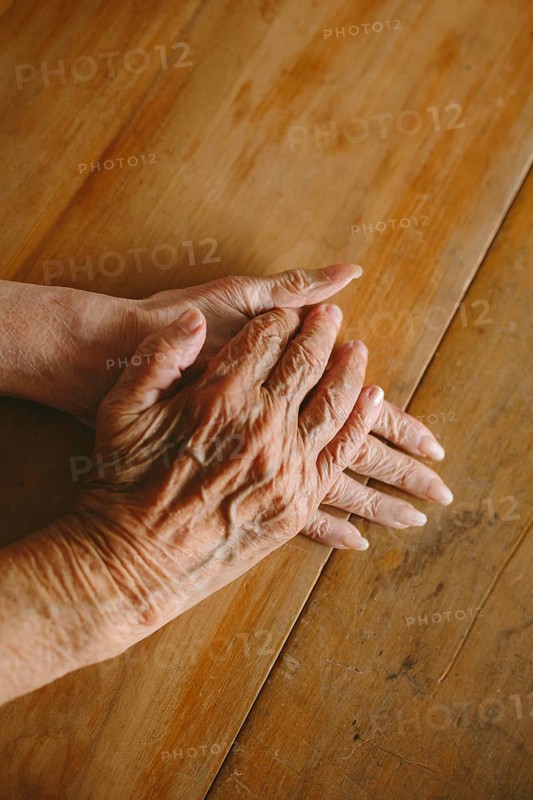 Close-up of elderly hands gently resting on a wooden table, capturing the texture and warmth of aging. Studio lighting enhances the details and shadows