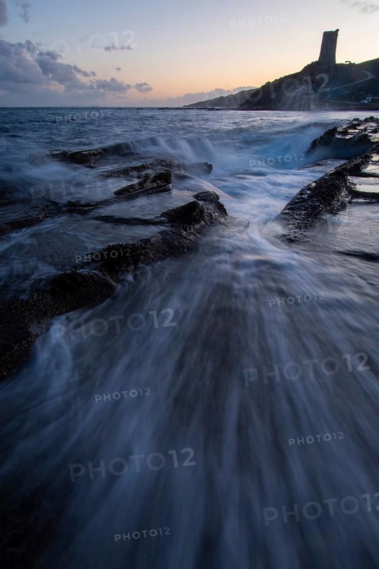 A mesmerizing sunset over the coast of Cadiz in Tarifa. Waves crash onto rocky shores as the sky transitions from day to dusk, creating a serene yet dramatic seascape