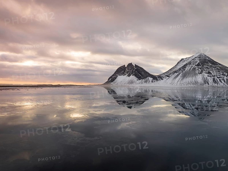 Stokksnes Beach in Iceland showcases stunning winter reflections. Snow-dusted peaks and tranquil waters create a breathtaking landscape, epitomizing Icelandic natural beauty