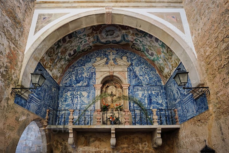 Historic chapel inside Porta da Senhora da Piedade in Obidos, with blue azulejo tiles, painted vault, stone archway and devotional niche in a medieval passage