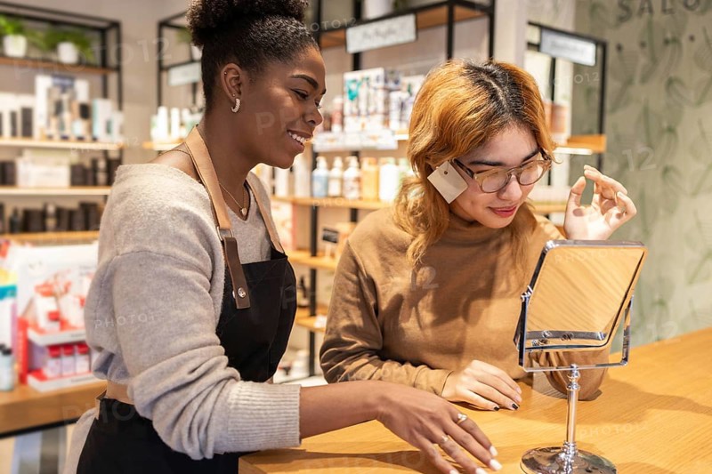 A employee in a cosmetics store help a customer with makeup. She is focused on providing excellent service, showcasing various beauty products in a friendly environment