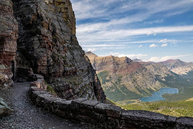 Rugged mountain landscape of Glacier National Park in Montana, showcasing dramatic cliffs, lush valleys, and a serene lake under a vibrant blue sky, perfect for adventure seekers