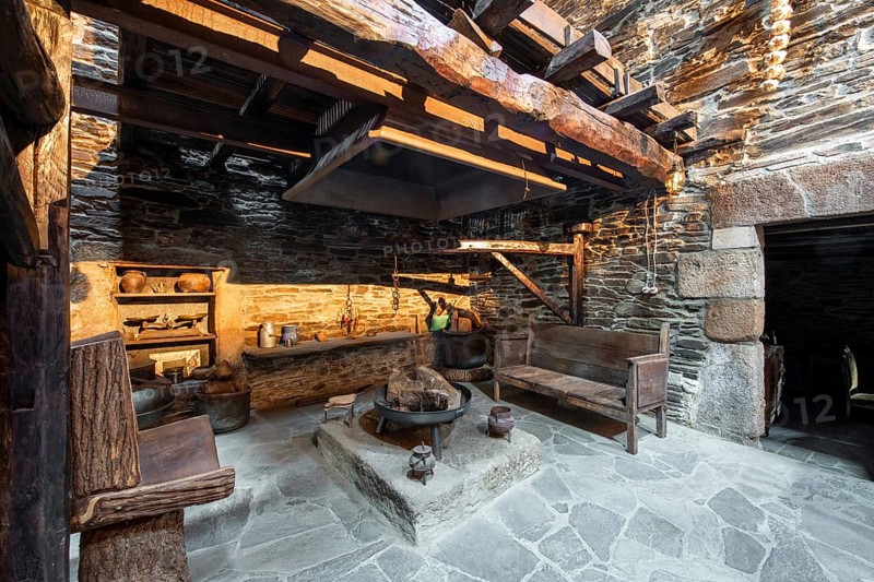 Traditional rustic kitchen inside a country house in Lugo, Spain, featuring stone walls, wooden beams, and antique utensils