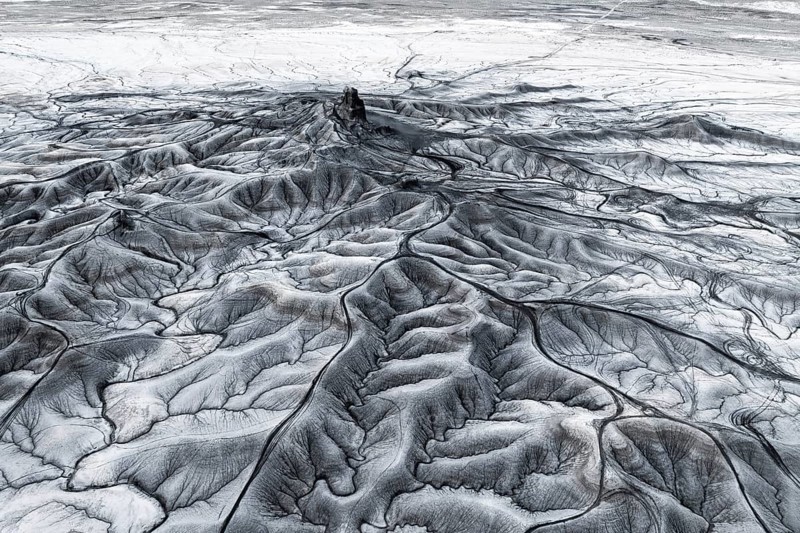 Aerial view of Moonscape Overlook in Utah showcasing intricate erosion patterns and stark geological textures in a barren landscape. The play of light and shadow emphasizes the rugged terrain and delicate formations typical of desert topography