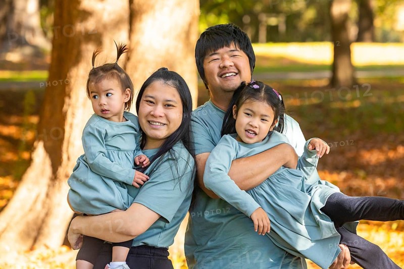 A joyful Asian family with parents and two young children, smiling and playing together in a sunny park. The warm atmosphere emphasizes love and togetherness in nature