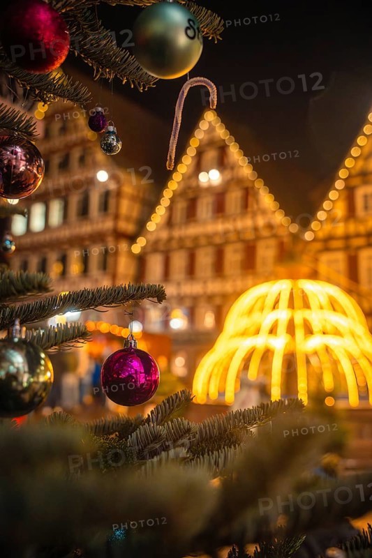 Close-up of Christmas baubles on a tree in front of a glowing structure and houses, Christmas market Calw, Black Forest, Germany