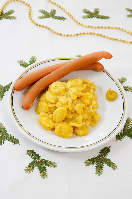 Swabian cuisine, potato salad with string sausages, Wienerle, Wiener sausages, thin boiled sausage, horseradish sausage, Frankfurter sausage, savoury, salty, typical Swabian, typical Christmas dinner, quick cuisine for Christmas Eve, home cooking, plate, mustard, Christmas decoration, golden chain on the back, hand-embroidered table linen, Christmas motifs, fir branch motif, Christmas tablecloth, handmade, traditional cuisine, food photography, studio, Germany